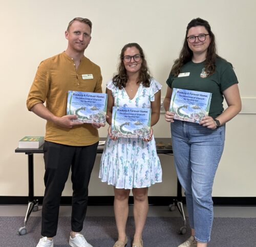 Three people holding children's book, "Finding A Forever Home", written by Dominique Rumball.